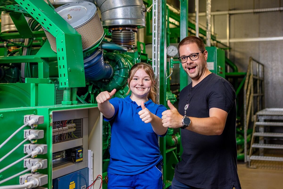 Azubine im Bereich Betriebstechnik mit Ausbilder. Foto: Salih Usta Symbolbild: Azubine mit ihrem Ausbilder vor einer großen Betriebsanlage mit Schaltkasten