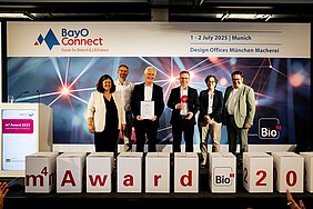 Die Preisträger mit Organisatorinnen und Staatssekretär auf der Bühne - davor sind Würfel mit Buchstaben m4 award
