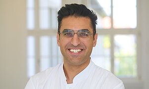 Porträtbild von Ugur Uslu mit Kittel im Flur der Dermatologie 