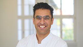 Porträtbild von Ugur Uslu mit Kittel im Flur der Dermatologie 
