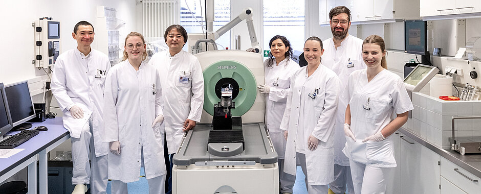 Das Team steht in weißen Kitteln und Hosen um einen PET-Scanner