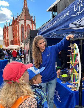 Am UKW-Stand steht eine Mitarbeiterin mit zwei Kindern am Glücksrad. Im Hintergrund ist die Kirche zu sehen.