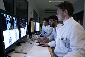 Prof. Buck mit zwei Mitarbeitern besprechen Bilder auf Monitore. 