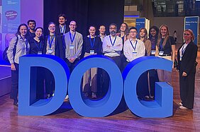 Mitarbeitende stehen hinter großen blauen 3D-Buchstaben DOG