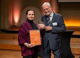 Kathleen Wermke hält auf der Bühne die Urkunde, Helmut Glück die gläserne Trophäe