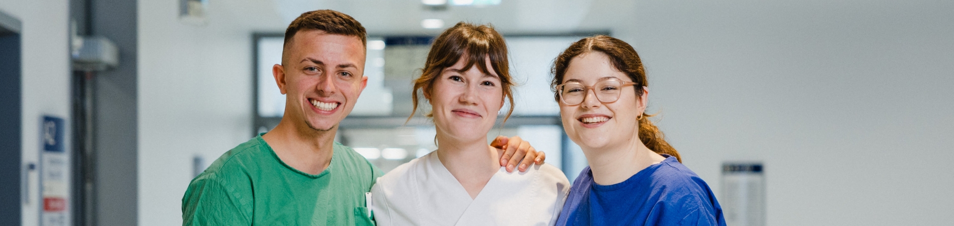 Station Team © UKW / Andreas Selter Drei Mitarbeitende einer Pflegestation stehen nebeneinander und lächeln