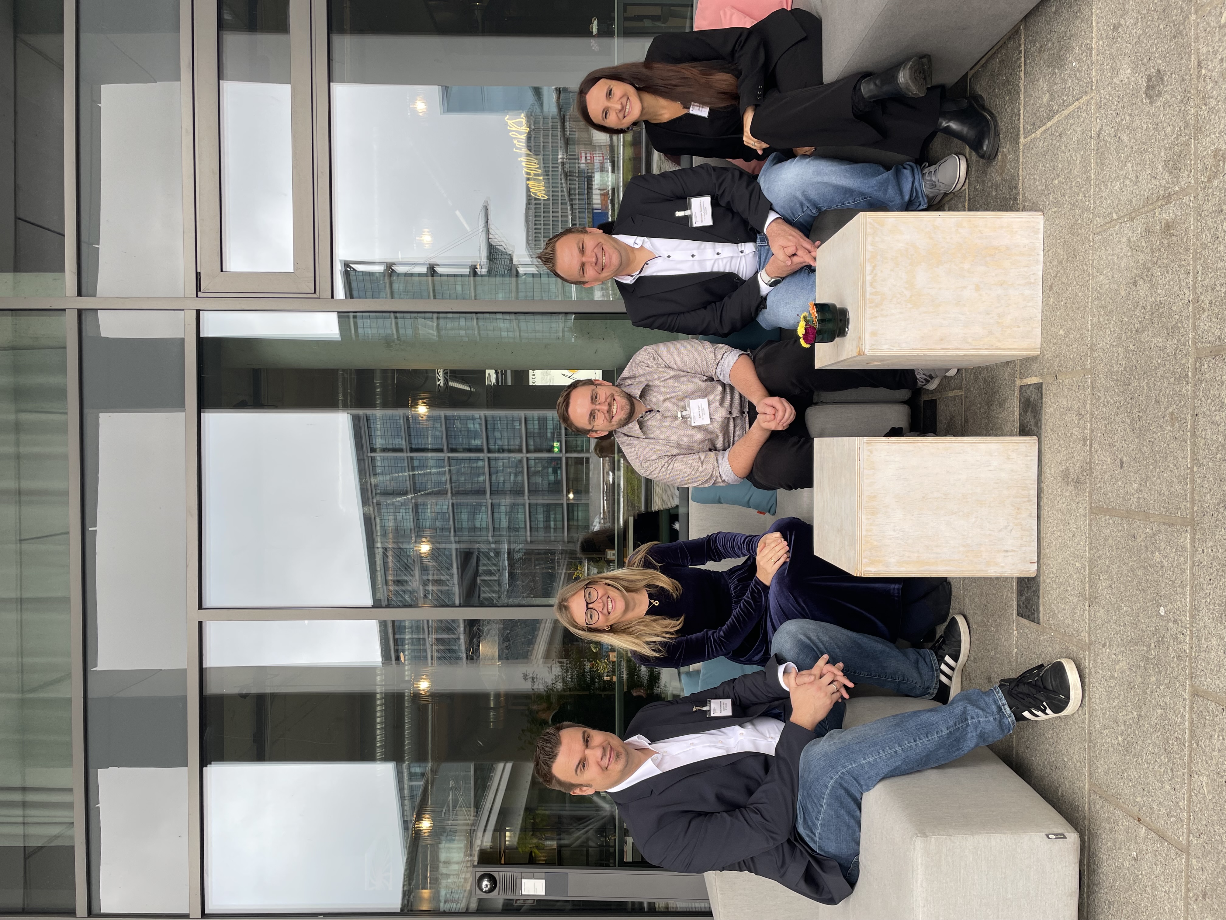 Prof. Dr.-Ing. Arne Rönnau, Prof. Dr. med. Astrid Schmieder, Dominik Beyer, Dipl.-Ing. Christoph Zimmermann und Dilara Diegelmann sitzen auf einem Sofa vor einer Gebäudefront aus Glas.