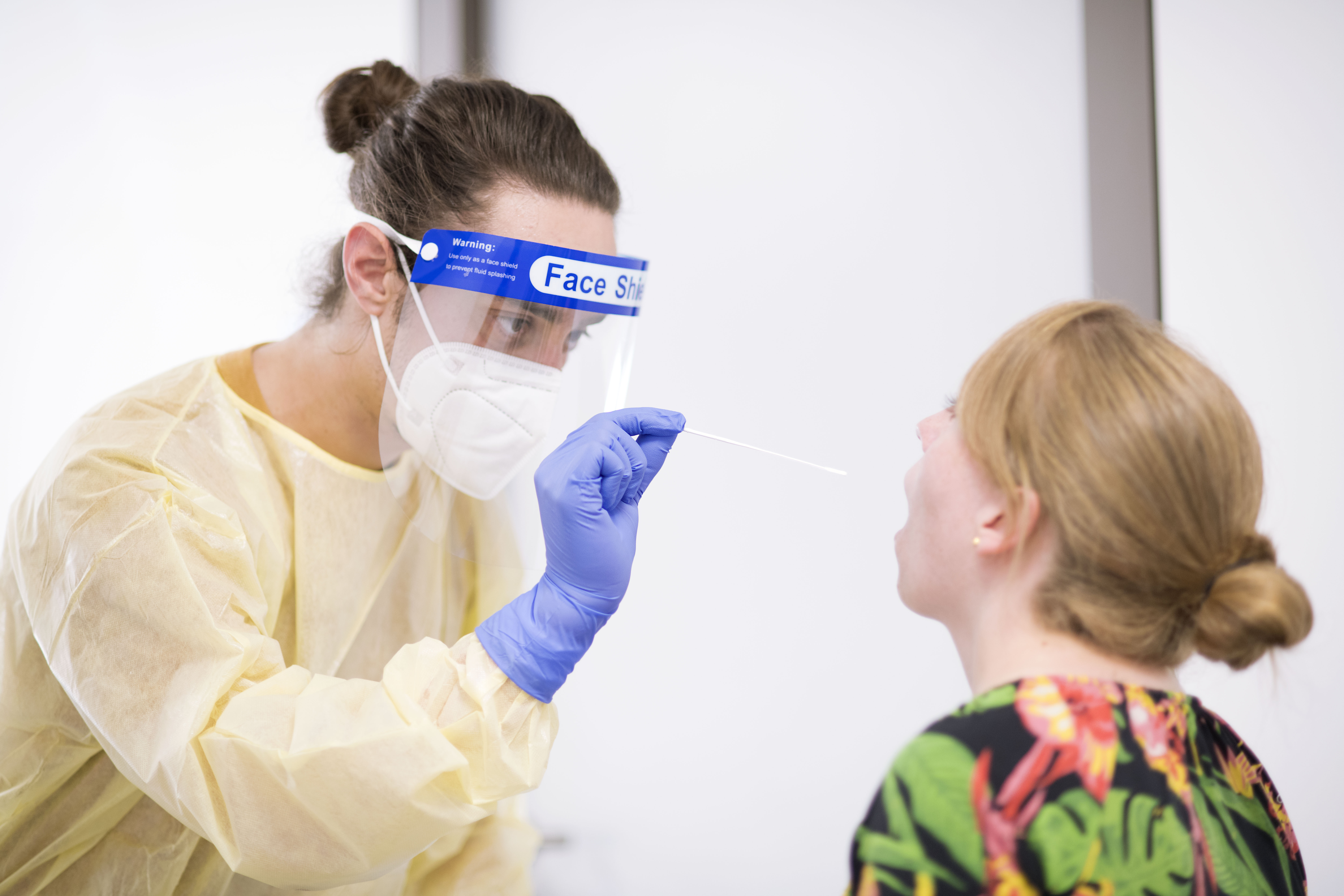 Das Bild zeigt eine Testsituation am Uniklinikum Würzburg, ein Mitarbeiter entnimmt mit einem Teststäbchen eine Speichelprobe bei einer Probandin. 
