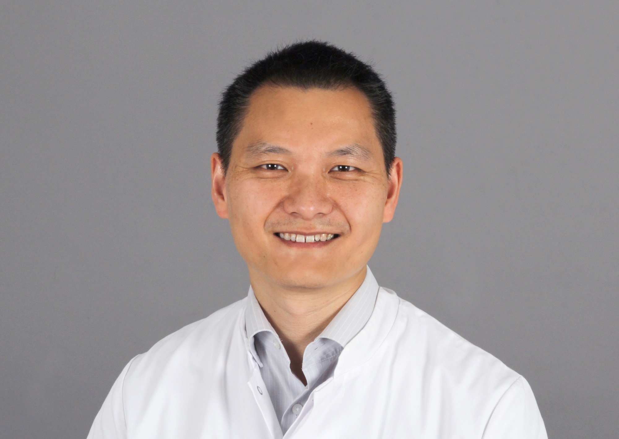 Porträtfoto von Chi Wang Ip im weißen Kittel vor grauem Hintergrund 