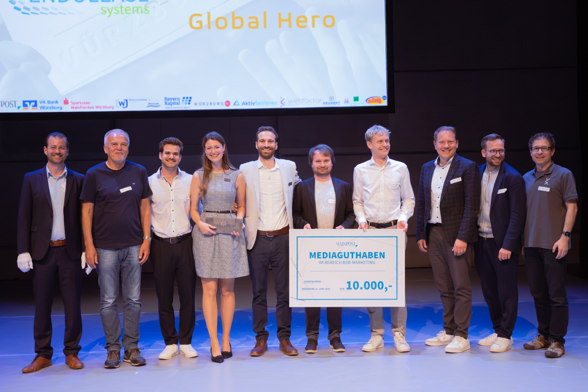 Die Preisträger und die Jury stehen auf der Bühne mit einem riesigen Scheck über 10.000 Euro für ein Mediabudget der Main-Post