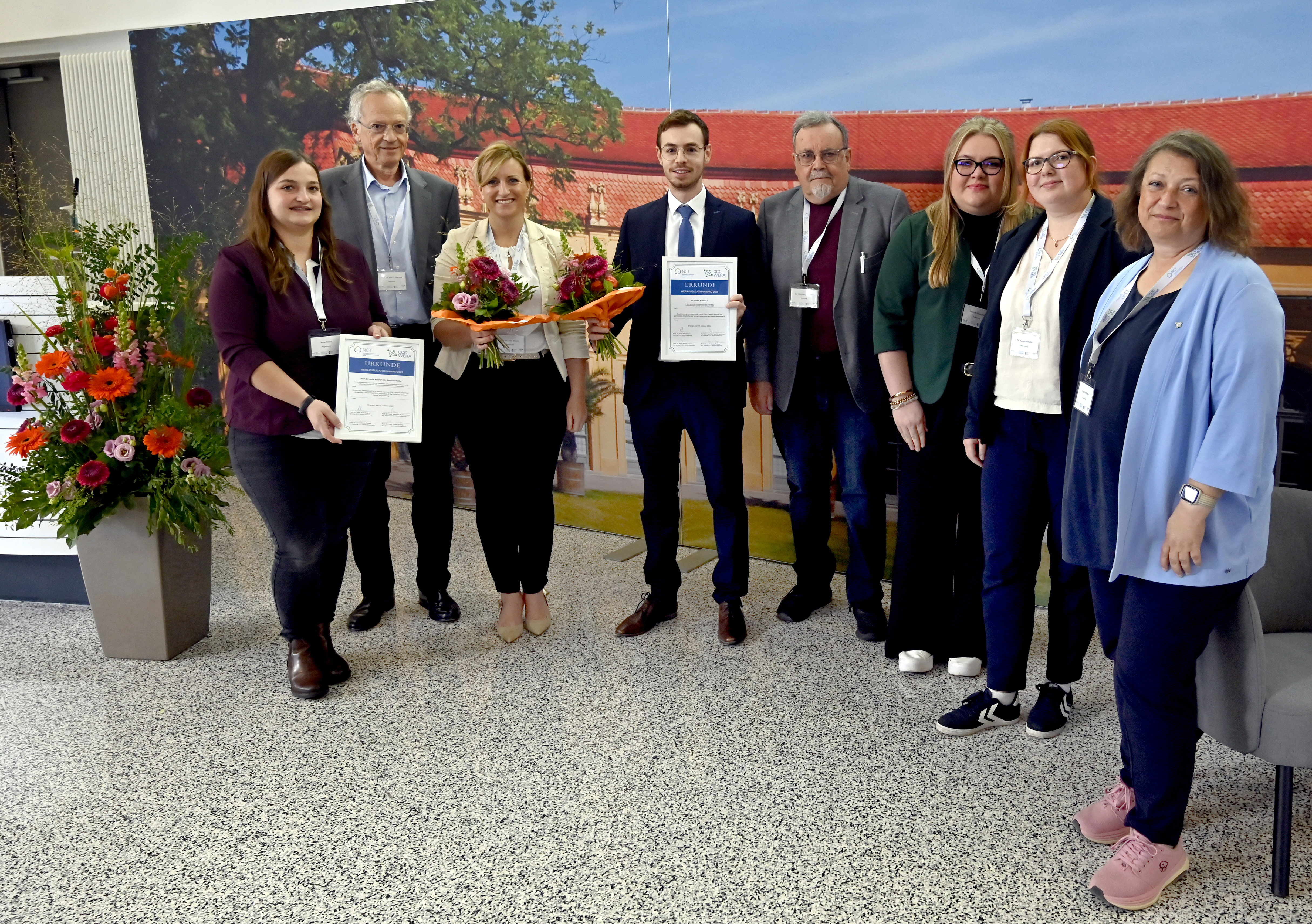 Preisträger und Preisträgerinnen mit Urkunde und Blumenstrauß umringt von Vertreterinnen und Vertretern des CCC und NCT WERA im Halbkreis vor einer Stellwand. 