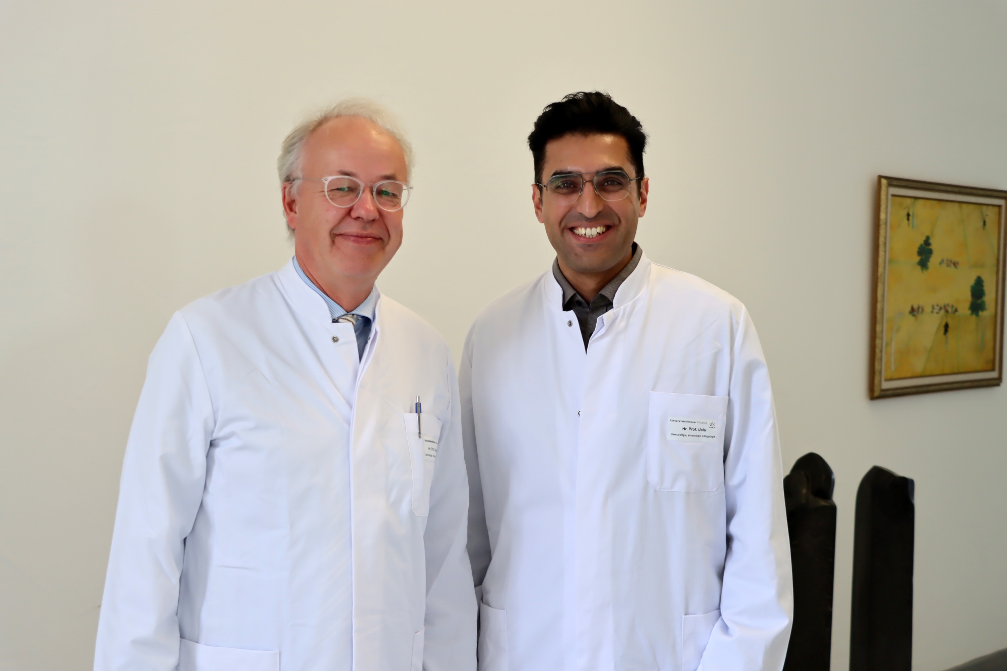 Matthias Goebeler und Ugur Uslu Matthias Goebeler und Ugur Uslu posieren in weißen Kitteln im Flur der Dermatologie