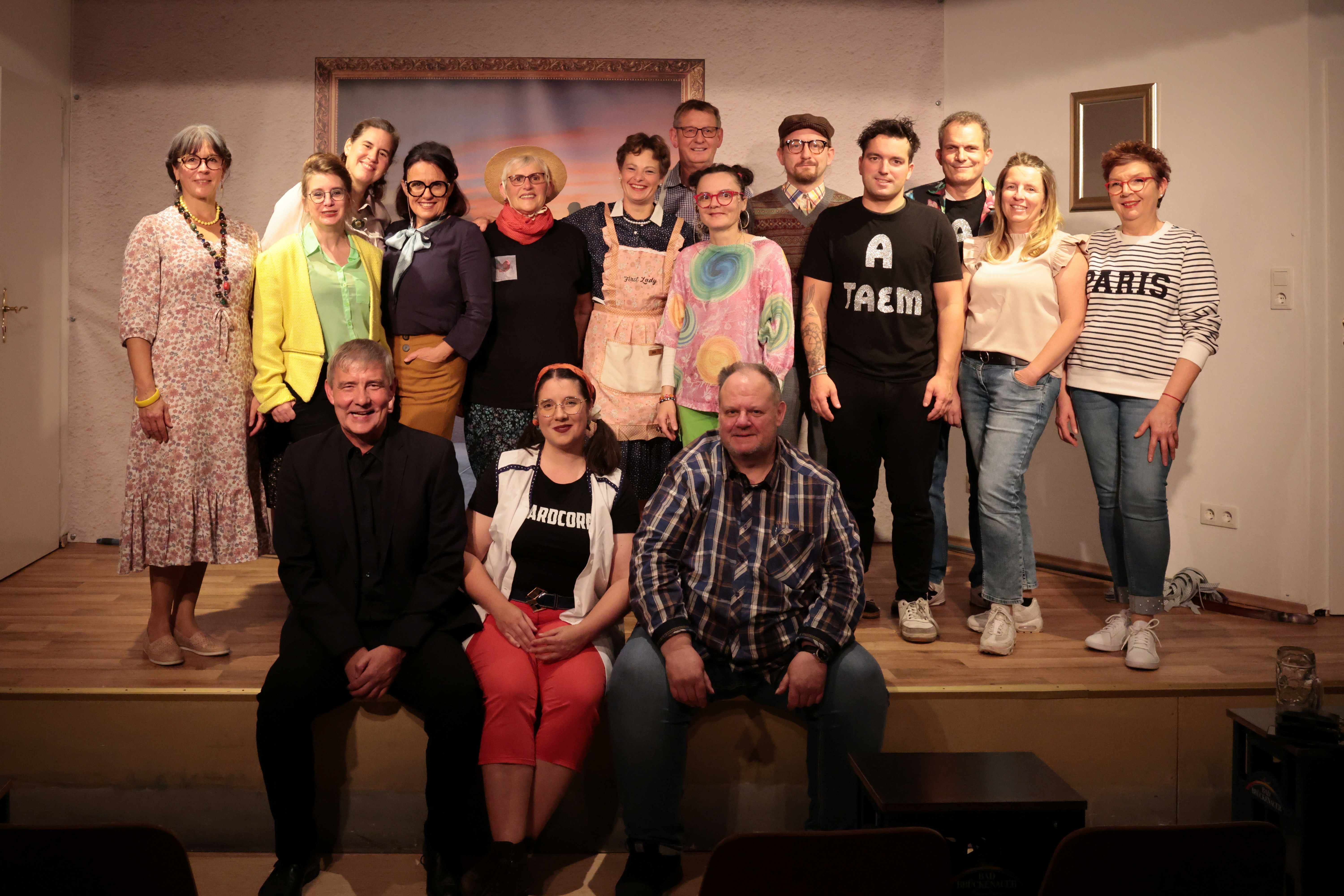 Auf dem Foto sieht man mehrere Personen, die teilweise verkleidet sind und auf einer Bühne stehen bzw. sitzen. 