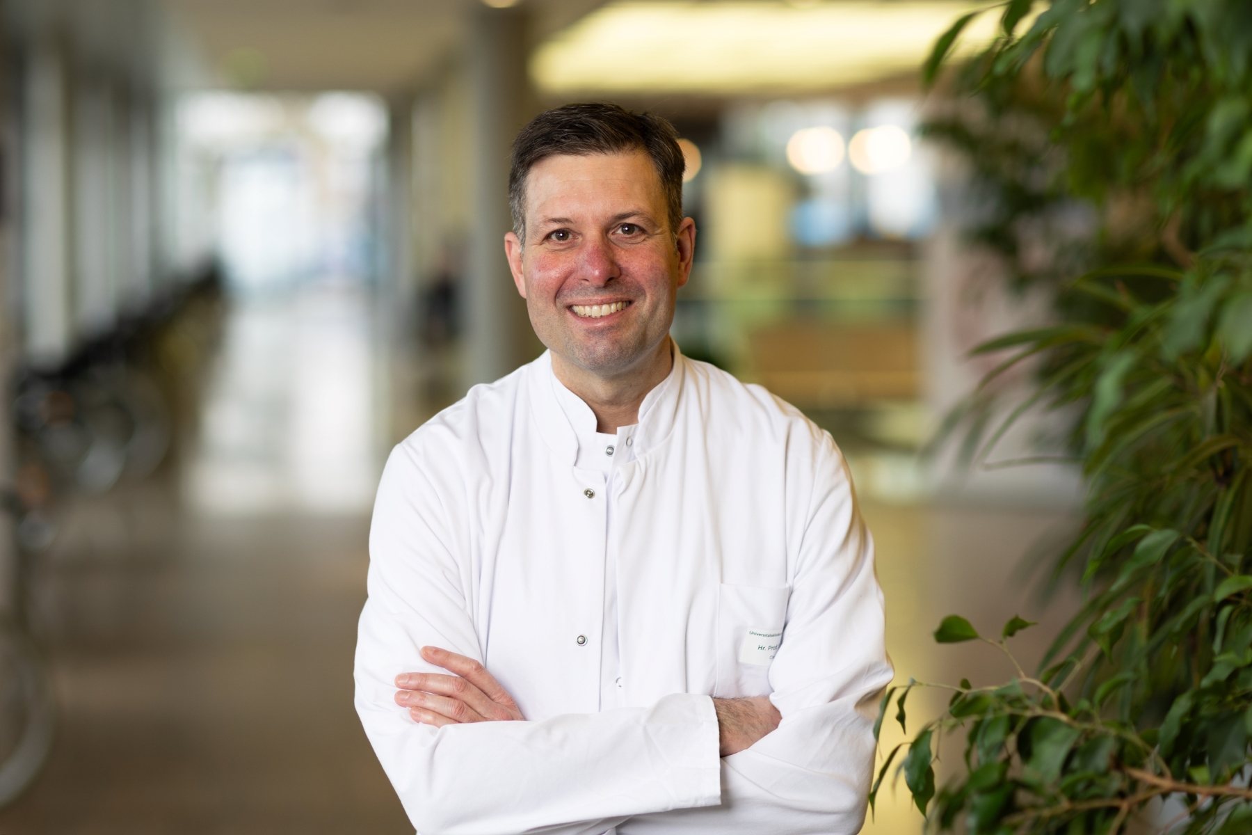 Porträt von Nicolas Schlegel im weißen Kittel mit verschränkten Armen im Flur des Zentrums für Operative Medizin 