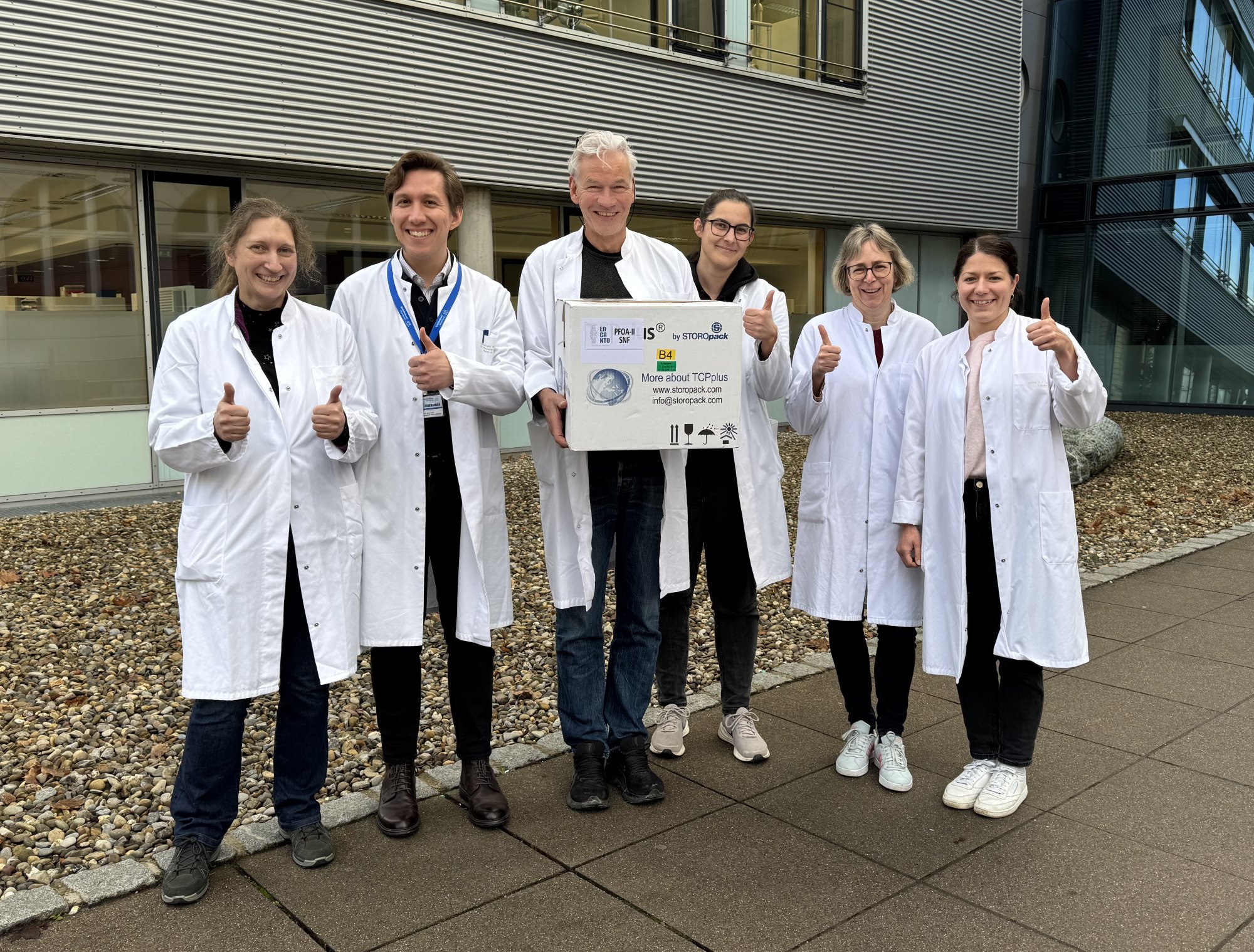 Die Mitarbeitenden stehen in weißen Kitteln vor der Zahnklinik und halten Karton hoch, der den Knorpel enthält. 