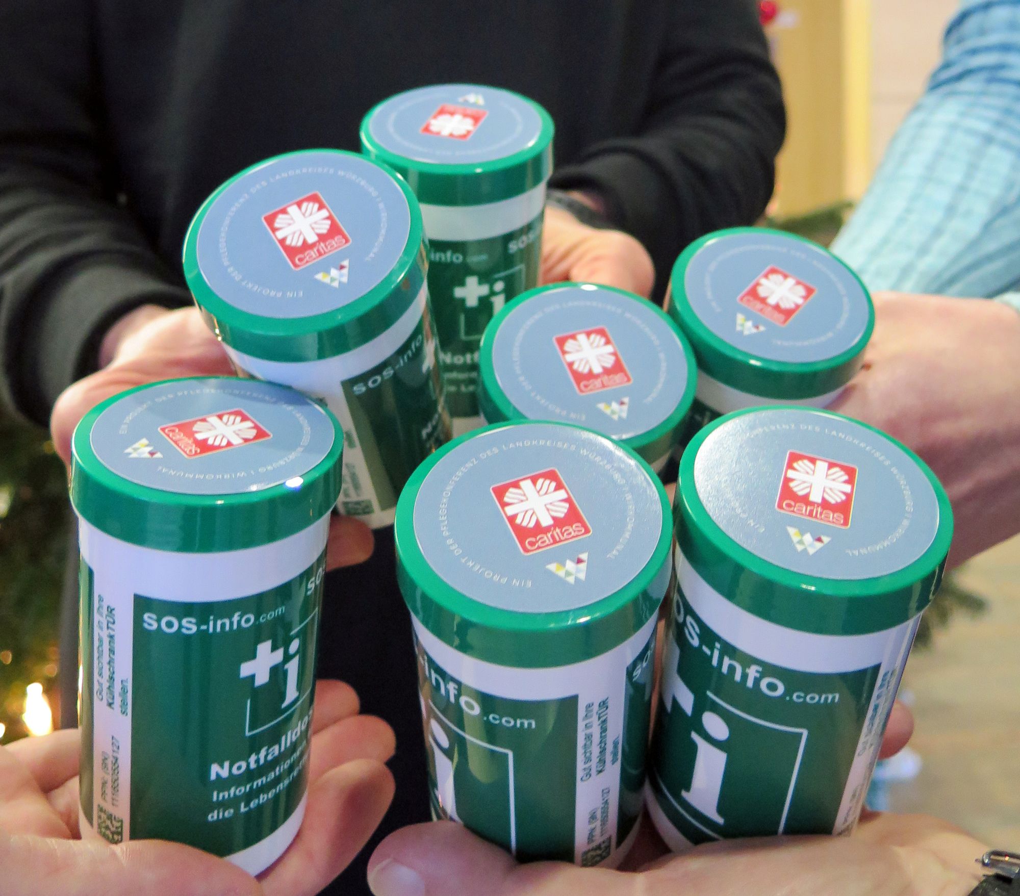 Auf dem Bild sieht man 7 Notfalldosen, die von mehreren Personen in der Hand gehalten werden. 