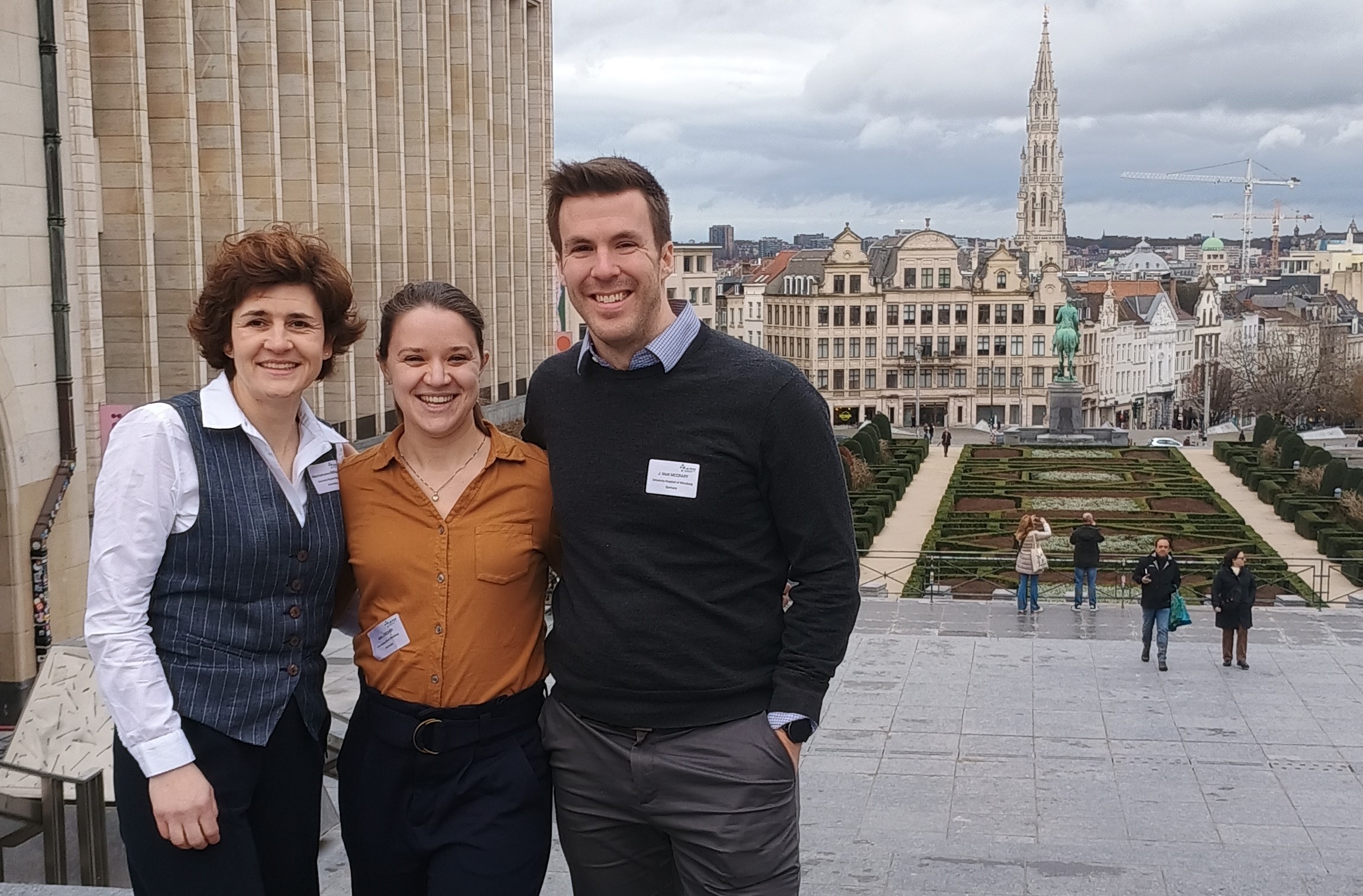 Die drei Forschenden stehen in Brüssel vor historischen Gebäuden.