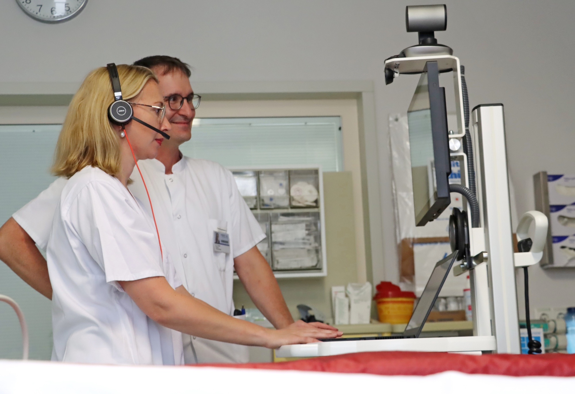Eine Ärztin und ein Arzt stehen in weißem Kasack vor einem Visitenwagen der Teleintensivmedizin.