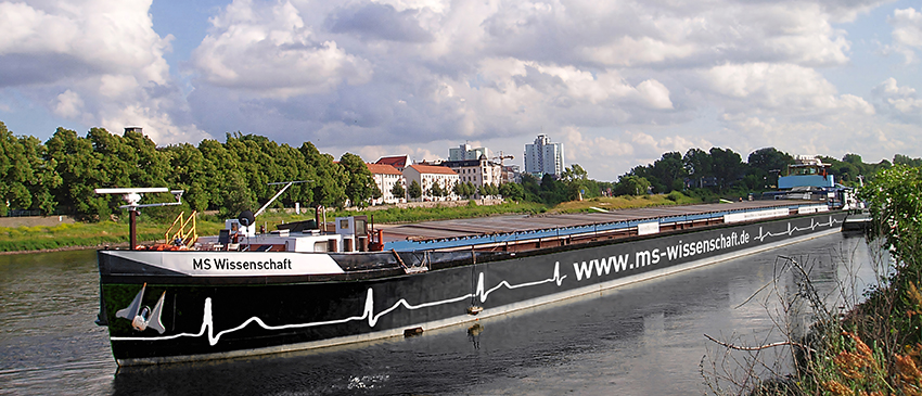 Das Boot mit schwarzem Rumpf fährt auf einem Fluss durch eine grüne Landschaft 