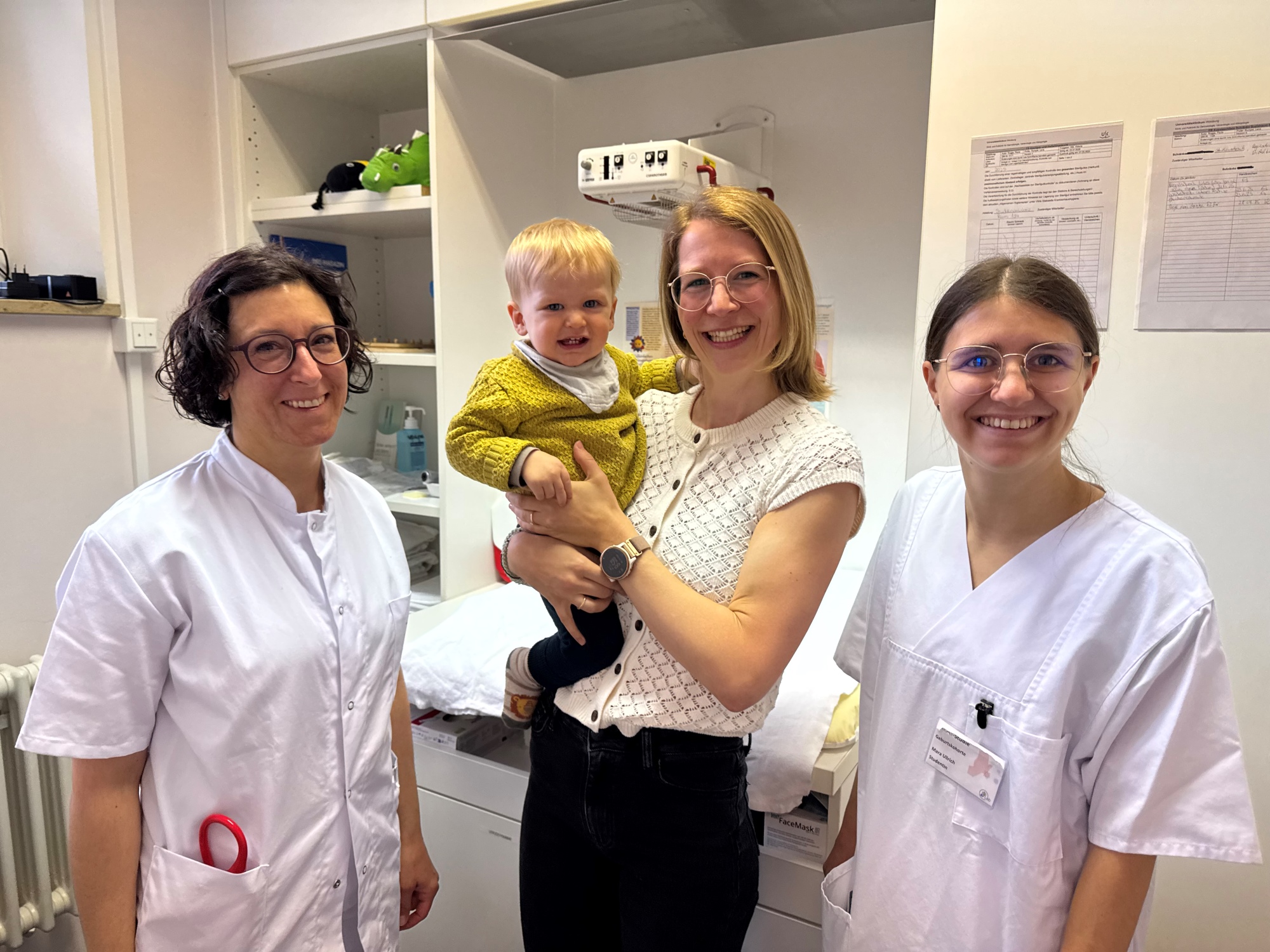 Die Mutter Hannah Hinz hält im Untersuchungsraum ihren Sohn auf dem Arm, daneben steht das Studienteam in weißer Kluft. 