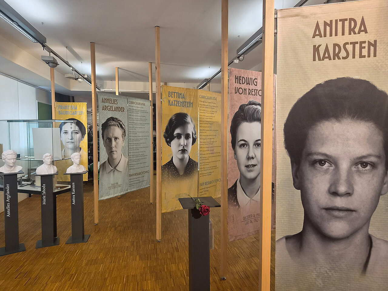 Ausstellung über Pionierinnen der Psychologie. Im Vordergrund auf einem Sockel liegt eine rote Rose und links stehen drei Sockel mit einer Büste. 