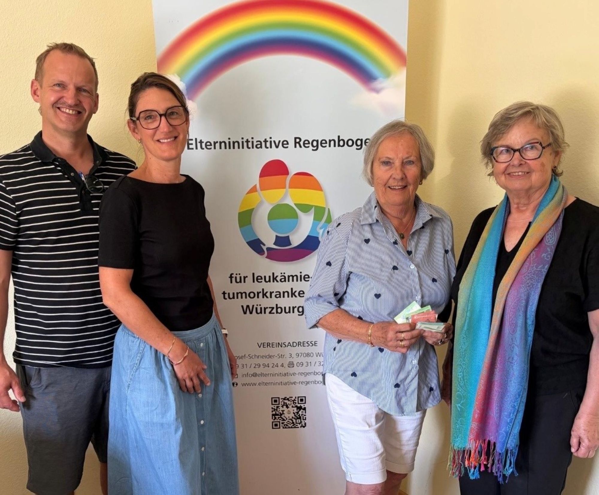 Gruppenfoto vor einem Aufsteller der Elterninitiative Regenbogen. Eine Frau hält Geld in der Hand.