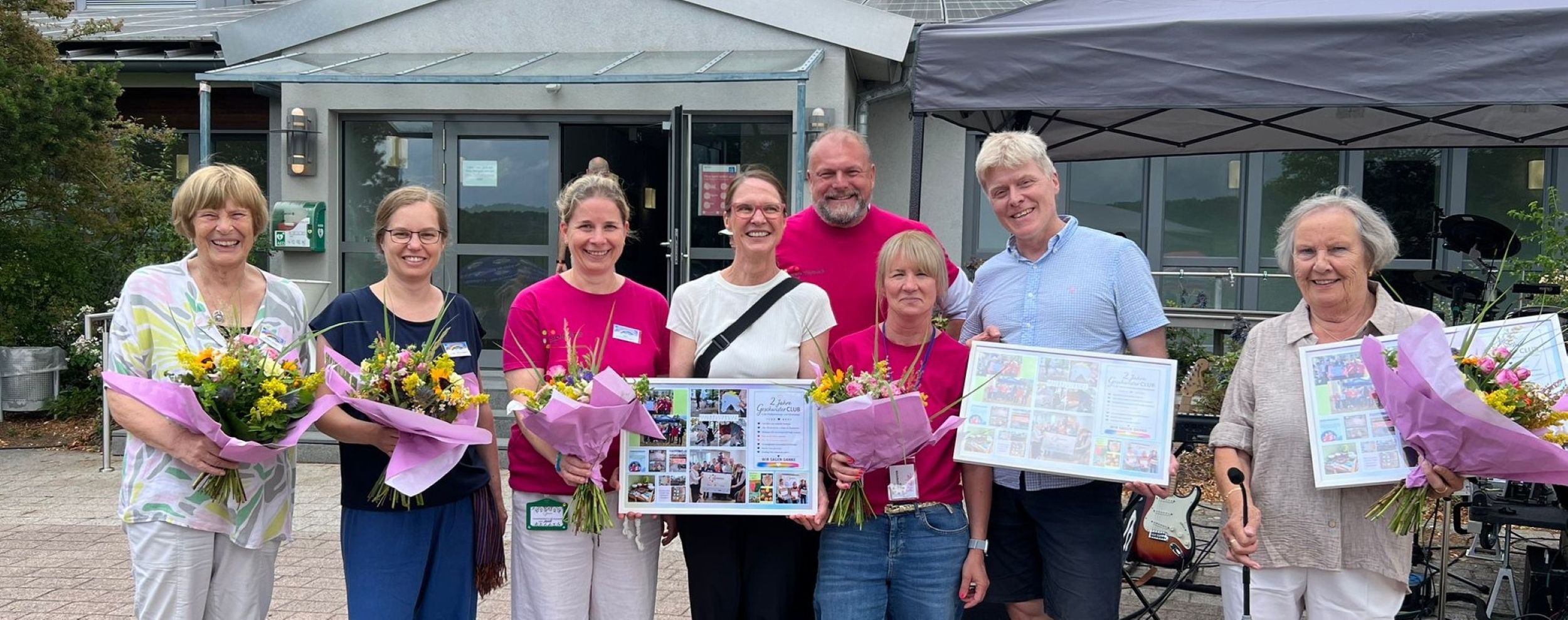 Gruppenfoto der Projektbeteiligten, welche Blumensträuße und Bilderrahmen halten.