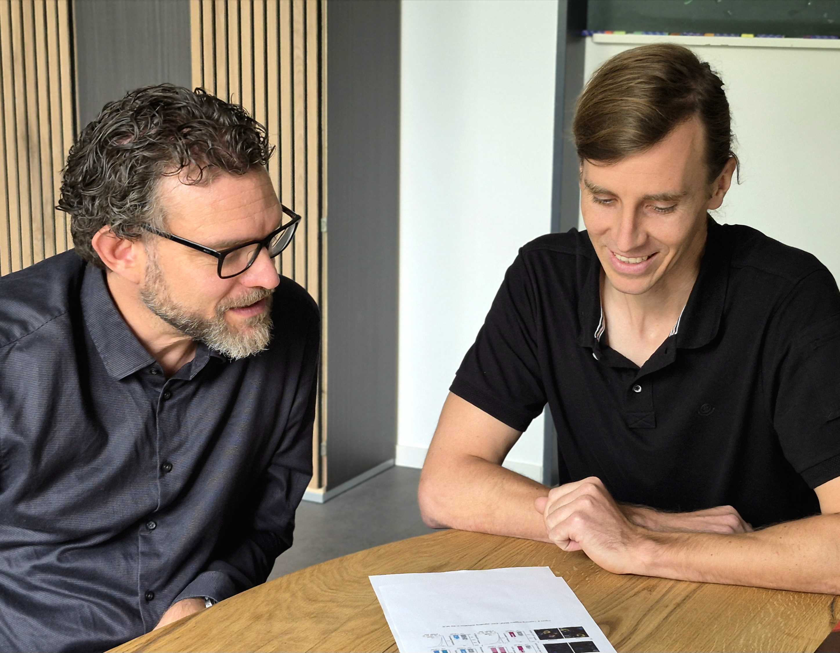 Die beiden Wissenschaftler sitzen am Tisch - vor sich der Ausdruck einer Publikation 