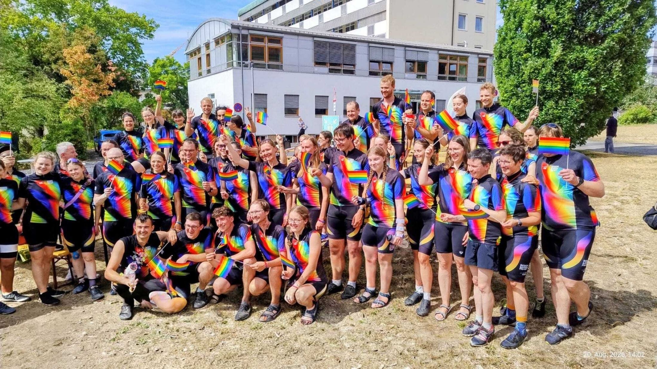 Gruppenfoto der Regenbogenfaher vor der Kinderklinik. Alle Teilnehmer haben ein T-Shirt mit Regenbogen an und teilweise auch mit Regenbogen-Fahnen. 