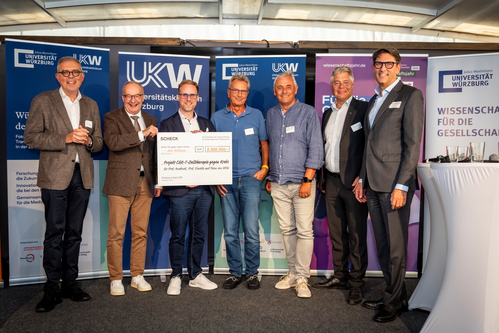 Sieben Männer stehen auf der Bühne der MS Wissenschaft, in der Mitte bzw. dritter von links Michael Hudecek mit Scheck in der Hand, im Hintergrund Roll-ups. 