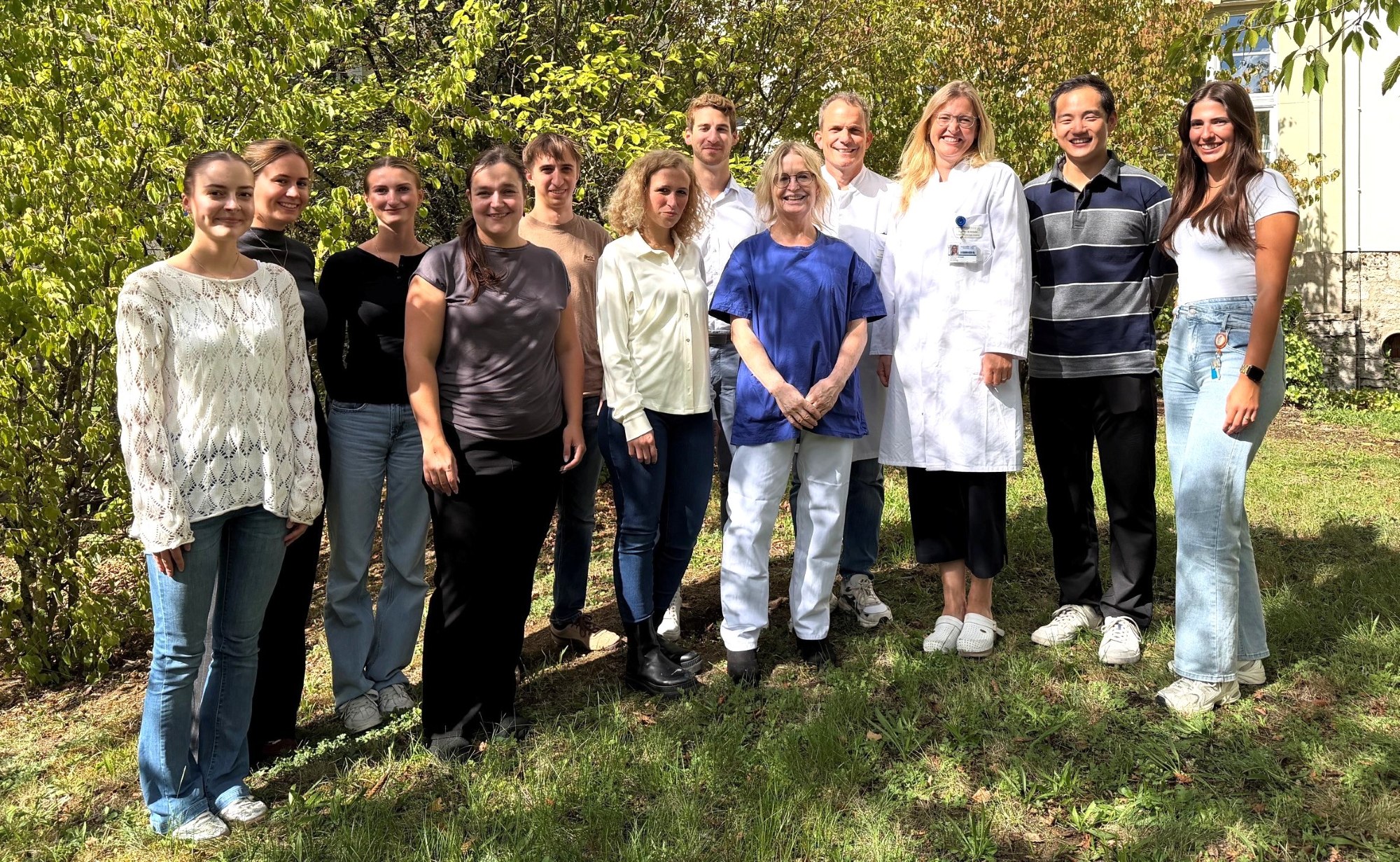 Das Team steht in zwei Reihen bei gutem Wetter unter Bäumen vor der Hautklinik. 