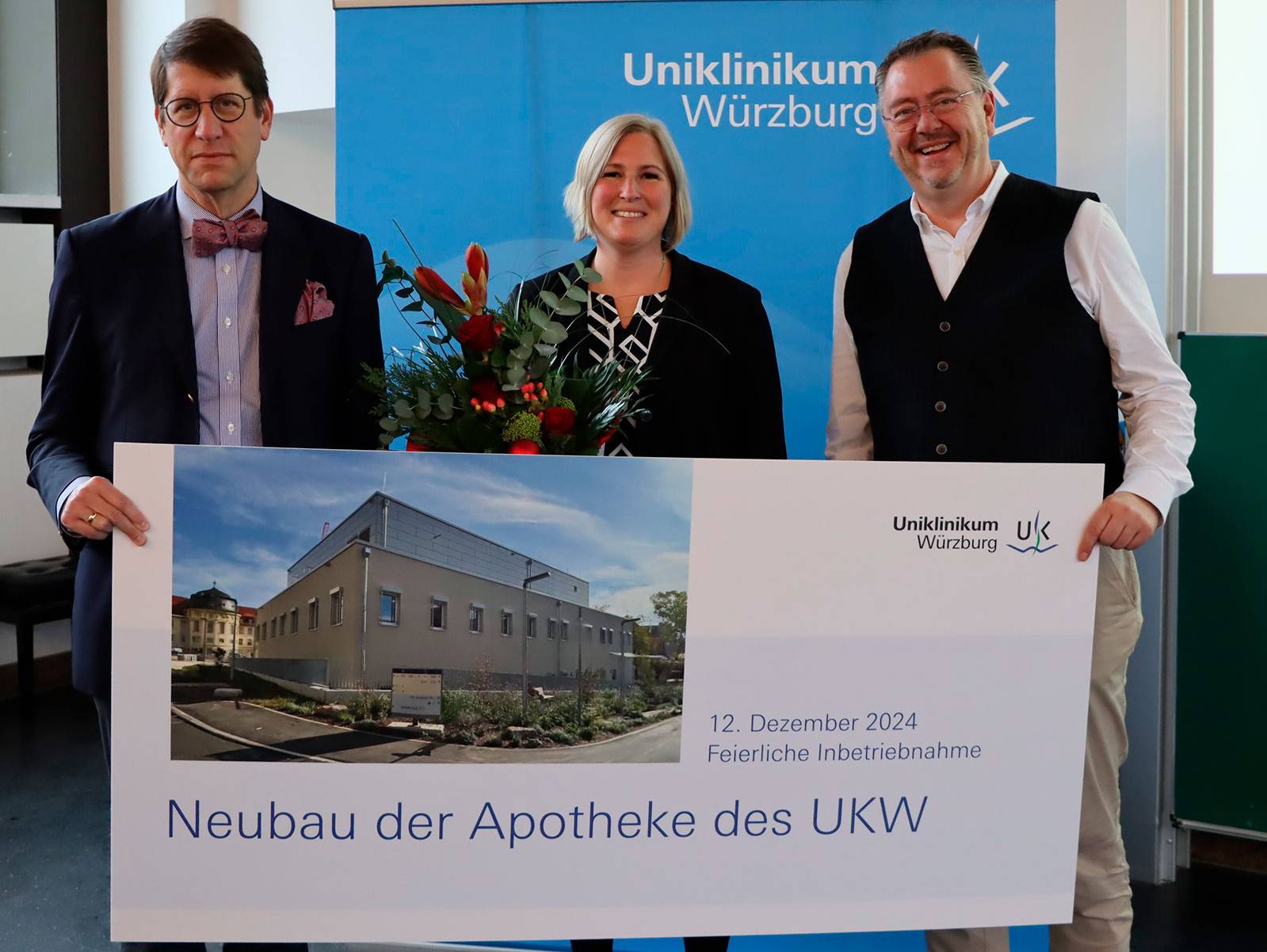 Drei Personen präsentieren ein Schild zur Eröffnung der neuen Apotheke des UKW am 12. Dezember 2024 in Würzburg.