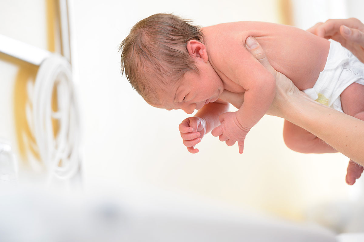 Säugling in Windel wird von Händen bäuchlings gehalten, weißer Hintergrund, Klinikumgebung