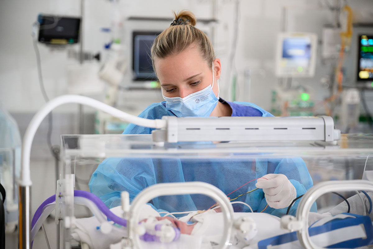 Fachpflegerin in Schutzkleidung ordnet Kabel in einem Inkubator auf einer Neugeborenenintensivstation