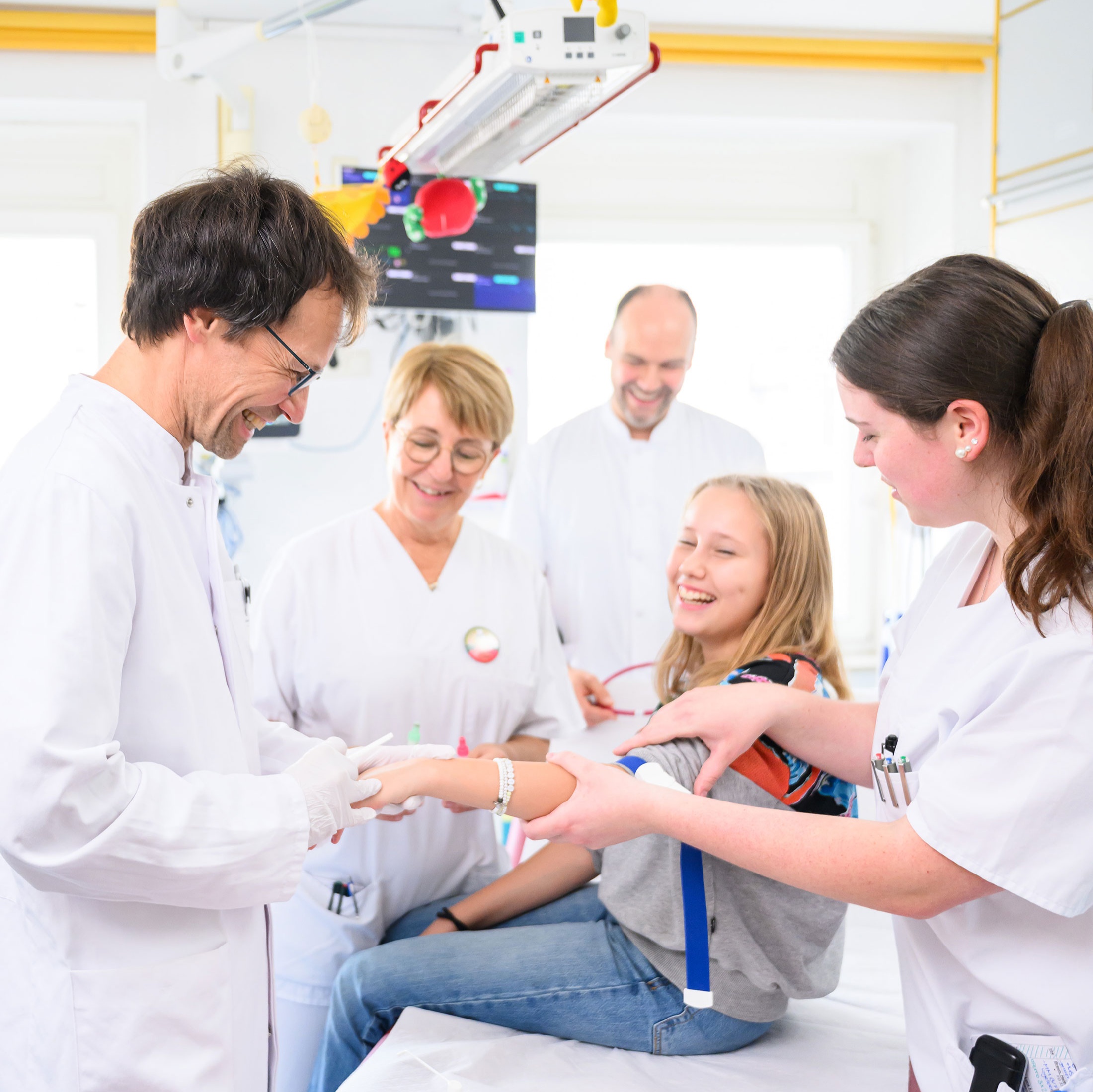 Team der Kinderklinik mit einem Mädchen, das eine Spritze bekommen soll. Alle lächeln.