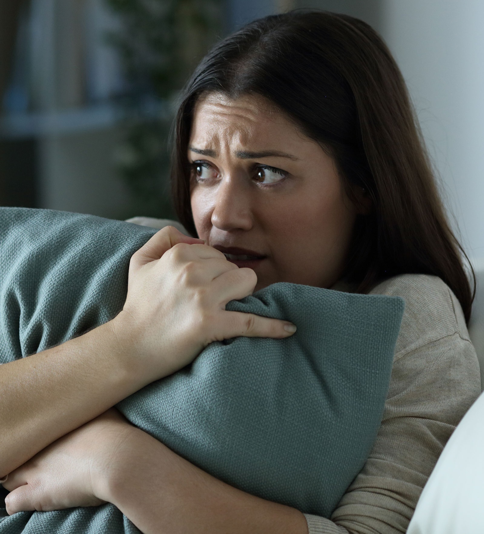 Eine verängstigt schauende Frau kauert sich zusammen und presst ein Kissen an sich.