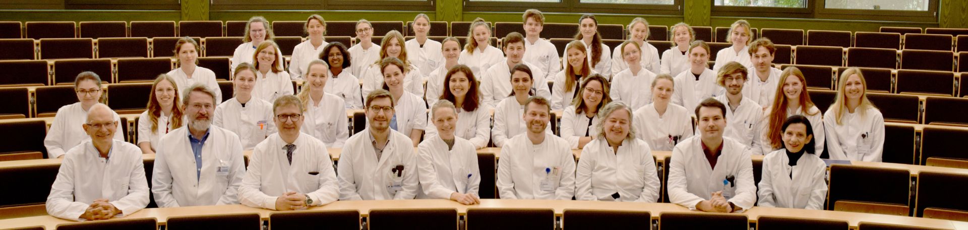 Das Team der Psychiatrie sitzt aufgereiht in einem Hörsaal und lächelt in die Kamera
