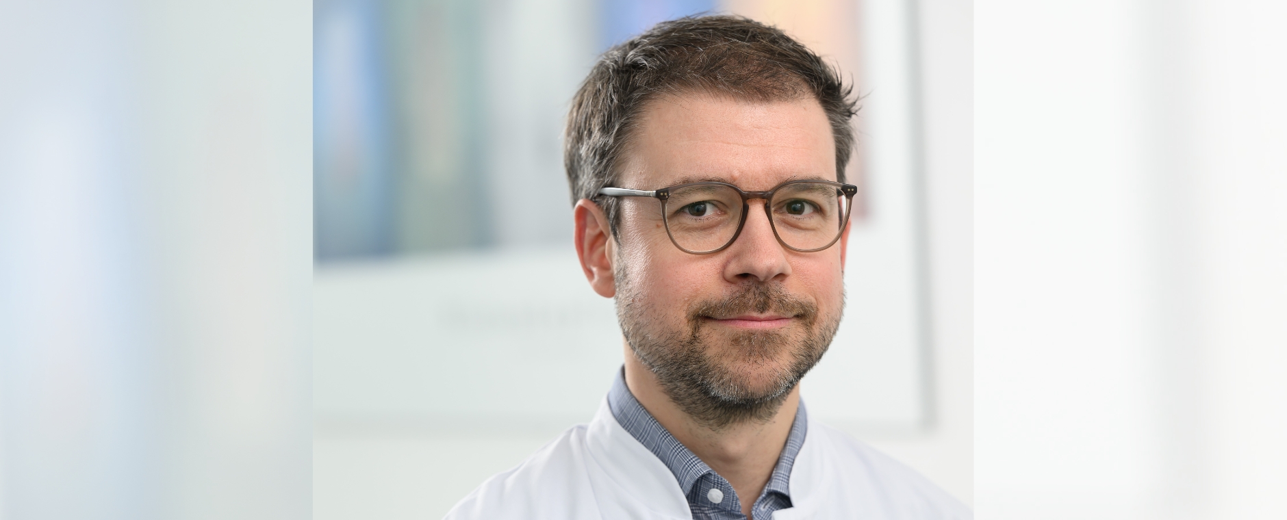 Porträt von Horst-Dieter Hummel - der Arzt und Wissenschaftler trägt weißen Kittel über einem grauen Hemd, braune Brille und Bart. 