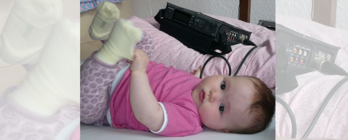 Zahnklinik ZVES - Baby mit Aufnahmegerät Das Bild zeigt ein liegendes Baby, das in die Kamera schaut - neben ihm ein Lautaufnahmegerät