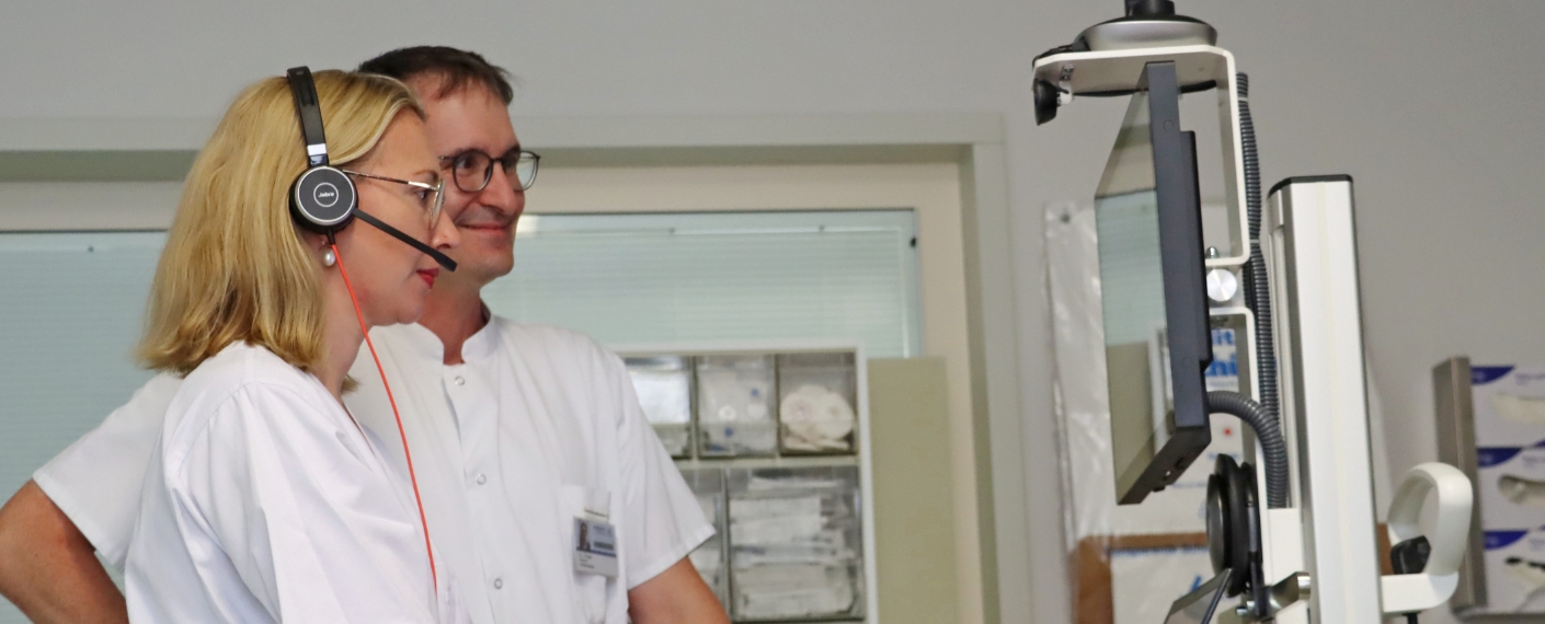 Zwei Mitarbeitende der Anästhesiologie stehen an einem Tele-Intensivmedizin-Wagen vorm Monitor 