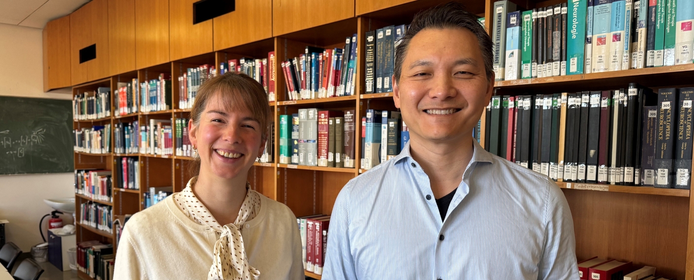 Lisa Harder-Rauschenberger und Chi Wang Ip stehen in der Bibliothek der Neurologie vor einem Bücherregal und schauen in die Kamera. 